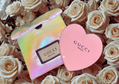 Gucci pink heart mirror displayed on a bed of white roses with an iridescent packaging